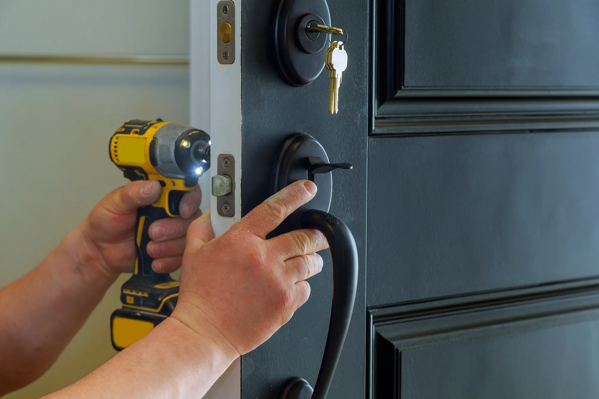 A person holding a drill and a screwdriver in front of a door.